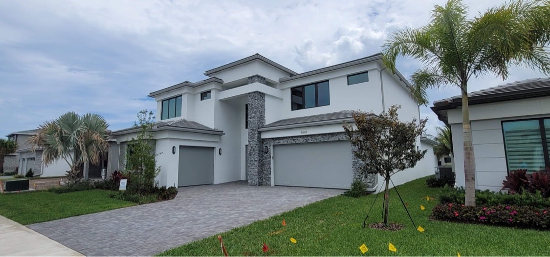Front exterior of 8804 Skyward Street — a two-story contemporary home in white stucco with a stone-veneer entry column, three-car garage, and paver driveway