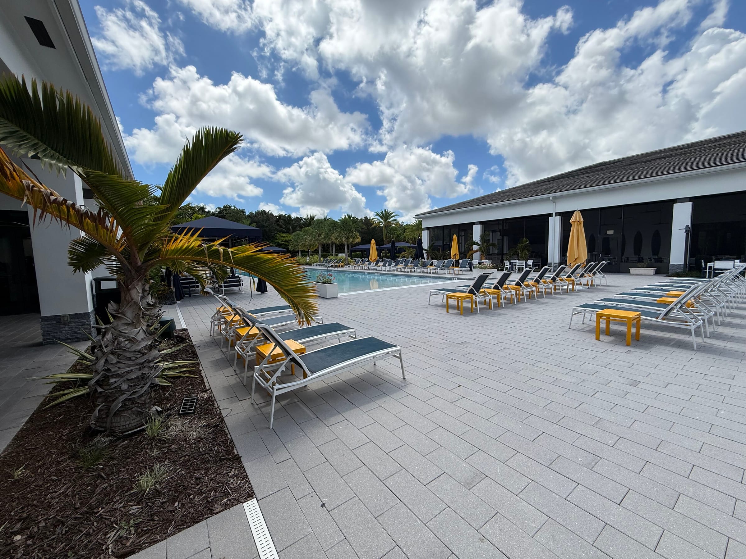 Resort pool and clubhouse building at Lotus Boca Raton, with loungers and cabanas along the paver deck