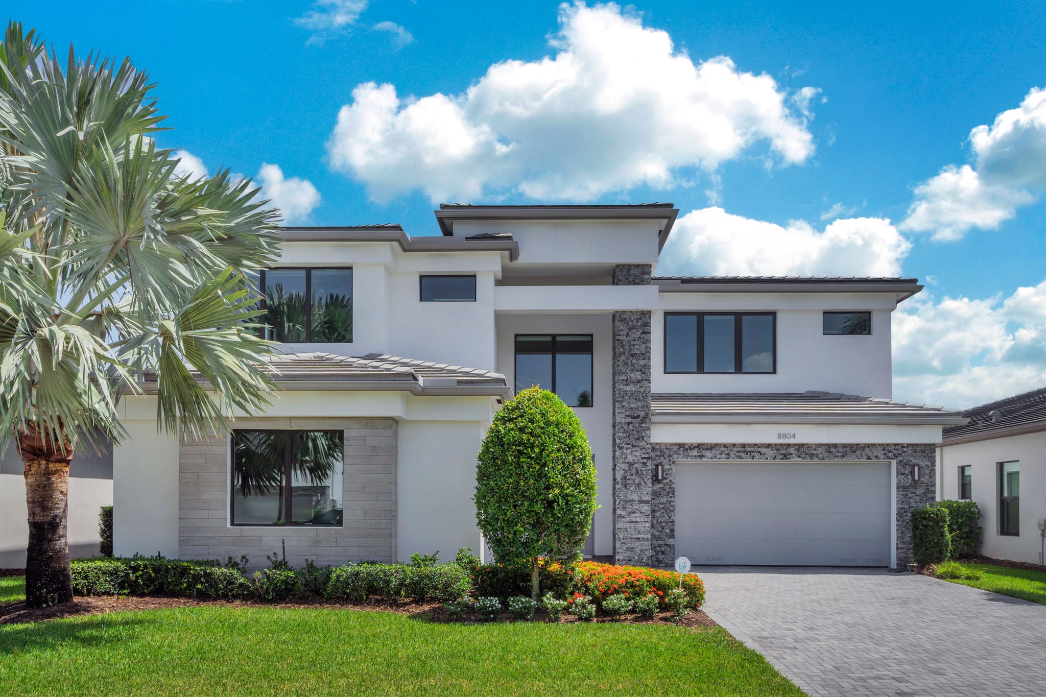 Front exterior of 8804 Skyward Street — a two-story contemporary home in white stucco with a stone-veneer entry column, three-car garage, and paver driveway